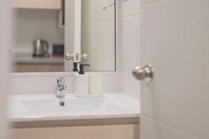 Une salle de bain avec un lavabo blanc, un miroir et une porte.