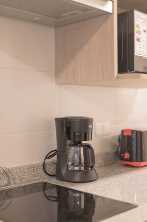 Une cuisine avec une machine à café sur le plan de travail, un four à micro-ondes au-dessus, et un appareil électroménager rouge sur la droite.