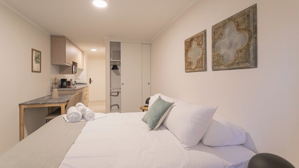 Habitación de hotel con cama, escritorio, silla, armario y dos obras de arte en la pared.