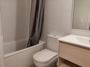 Un baño con inodoro, ducha con cortina y lavamanos con espejo.