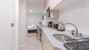 Habitación de hotel compacta con kitchenette, una cama y una pequeña zona de estar.