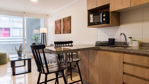A modern kitchen with wooden cabinets, a granite countertop, and a dining area with a table and chairs. - Santiago: 1BR Apartment with Balcony and Views (Santiago)