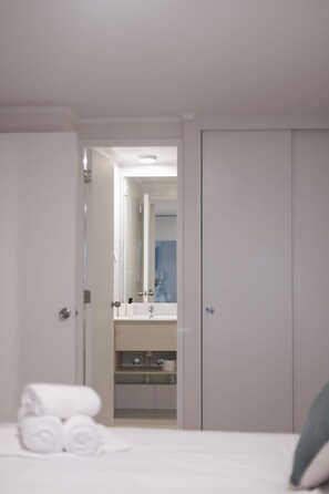 Bright bedroom with crisp white bedding, rolled towels, and a mirrored view of the clean vanity area. - Cozy Family-friendly Apt. in Santiago with Balcony (Santiago)