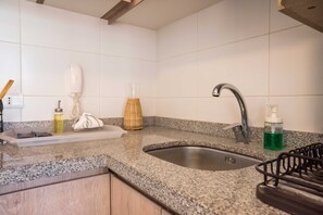 Una cocina con encimera de granito, pileta de acero inoxidable y estante metálico negro.