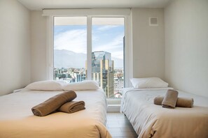 Habitación de hotel con dos camas, ventanas amplias y vistas a la ciudad.