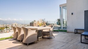 A rooftop terrace with a dining table and chairs, a bench, and a glass door leading to an outdoor area. - Stylish Modern City Flat | Prime Urban Experience (Santiago)