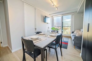 Un coin repas avec une table dressée pour quatre personnes, un téléviseur à écran plat fixé au mur et une vue sur la ville, visible à travers la porte-fenêtre coulissante.