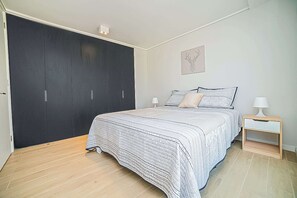 A bedroom with a large dark wardrobe, a bed with striped bedding, and a small bedside table with a lamp. - Functional and Bright Apartment in Providencia (Santiago)
