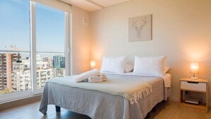 A bedroom with a large window, a bed with white linens, a bedside table with a lamp, and a wall-mounted artwork. - Modern Industrial Loft | Cozy Providencia Style (Santiago)