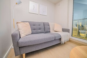 A grey sofa with cushions, a floor lamp, and framed pictures on the wall.