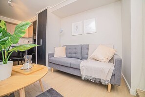 A modern living room with a grey sofa, a coffee table, a potted plant, and a kitchen in the background.