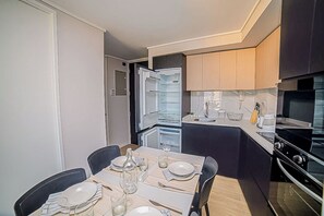 A compact kitchen with a dining area, featuring a built-in oven, a refrigerator, and a dining table set for four.