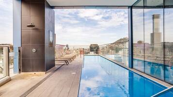 A rooftop pool with a clear view of the city skyline, a modern architectural design, and a glass railing.