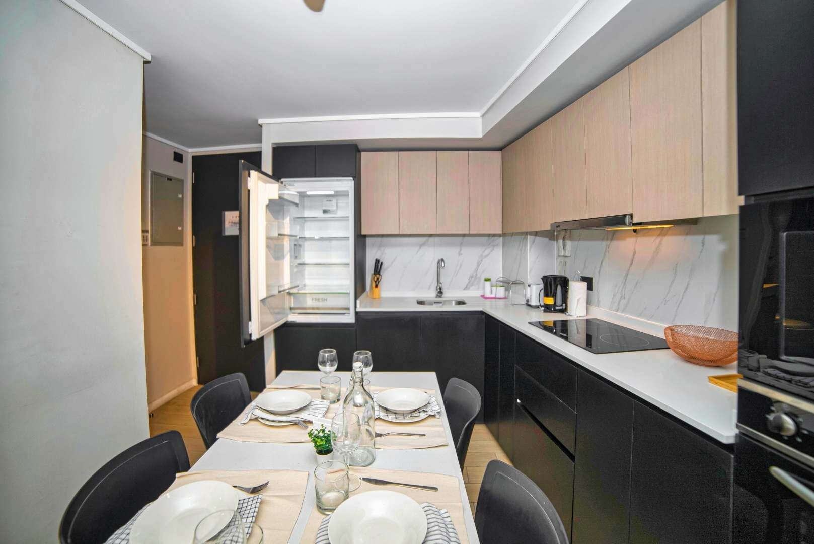 Een moderne keuken met een ingebouwde oven, een eettafel gedekt voor vier personen en een koelkast met een 'FRESH' label.