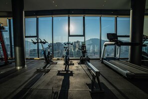 A gym with exercise equipment, large windows, and a view of a cityscape. - Premium experience in the heart of Providencia (Santiago)