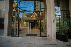 A building entrance with glass doors, a neon sign, and a potted plant.