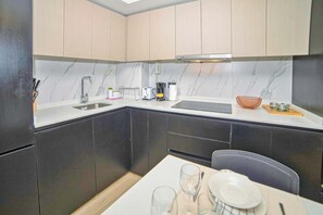 A compact kitchen with dark cabinets, a white countertop, a sink, and a dining area with a table set for two.