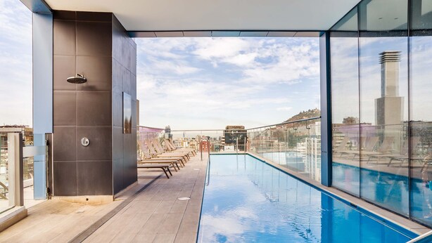 A rooftop pool with a clear view of the city skyline, a modern architectural design, and a glass railing.