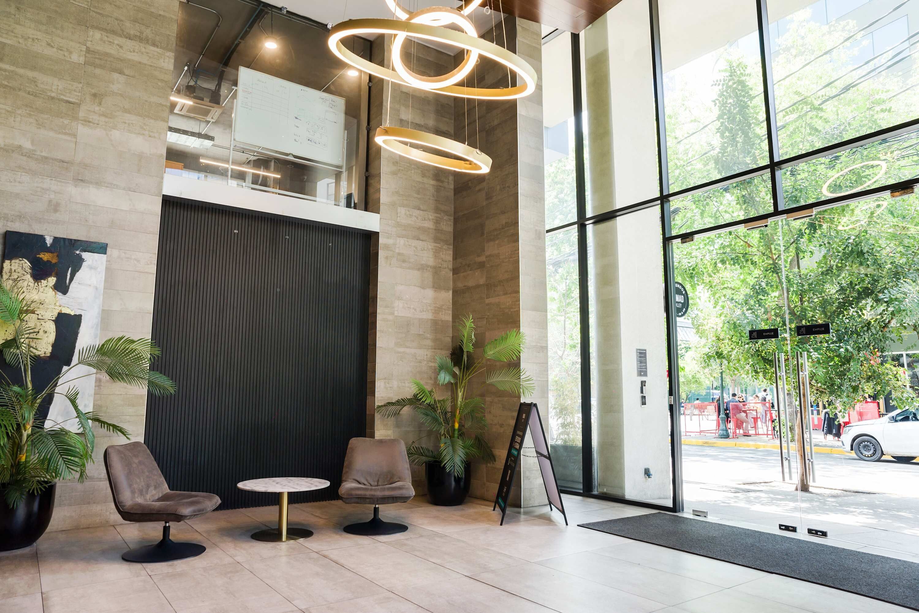 A modern lobby with two leather chairs, a round table, a whiteboard, and a large window with a view of the street.
