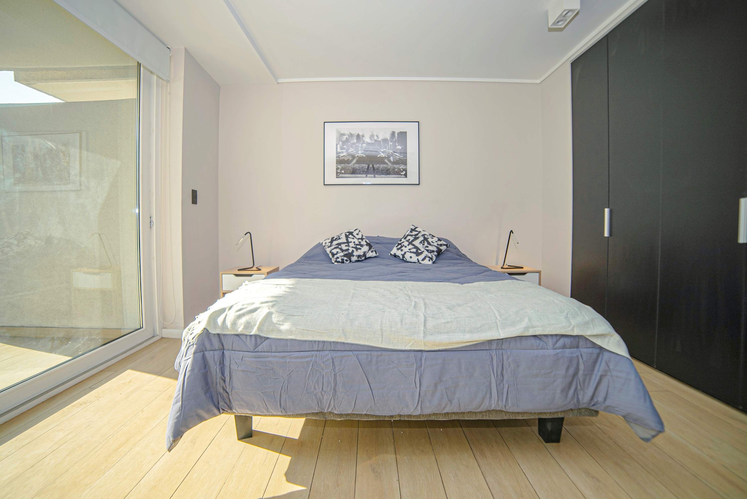 A modern bedroom with a large bed, a cityscape picture on the wall, and a sliding glass door.