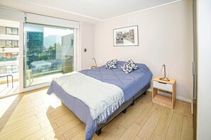 A modern bedroom with a bed, a bedside table, a hanging lamp, and a large window with a view of a cityscape.