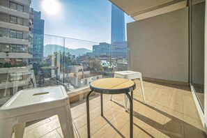 Un balcón con vistas a un paisaje urbano, una mesa redonda y dos taburetes blancos.