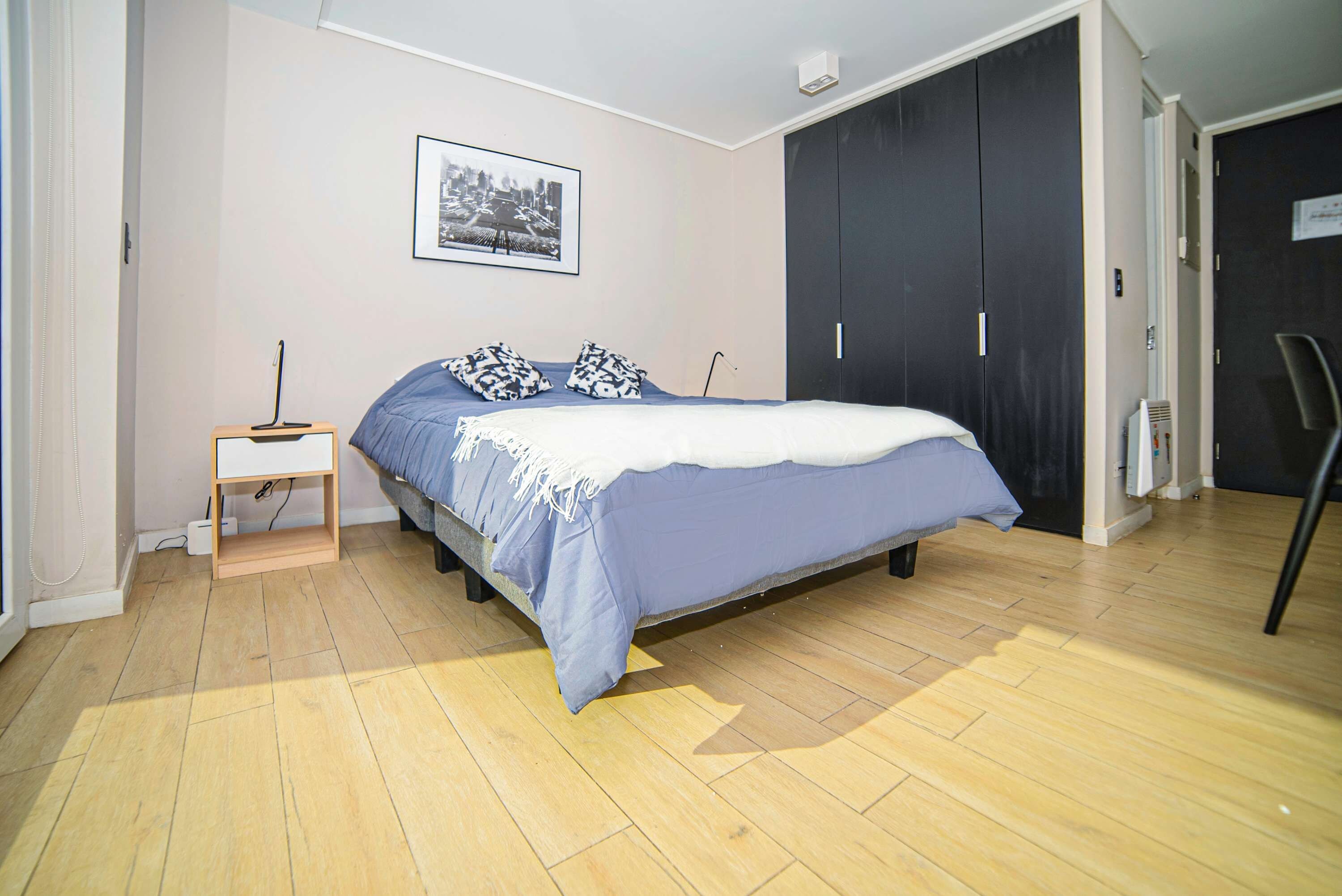 Een slaapkamer met een bed, nachtkastje, garderobe en een ingelijste foto aan de muur.