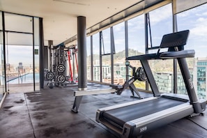 Une salle de sport équipée de tapis de course, d’appareils de musculation et offrant une vue sur le paysage urbain grâce à de grandes fenêtres.