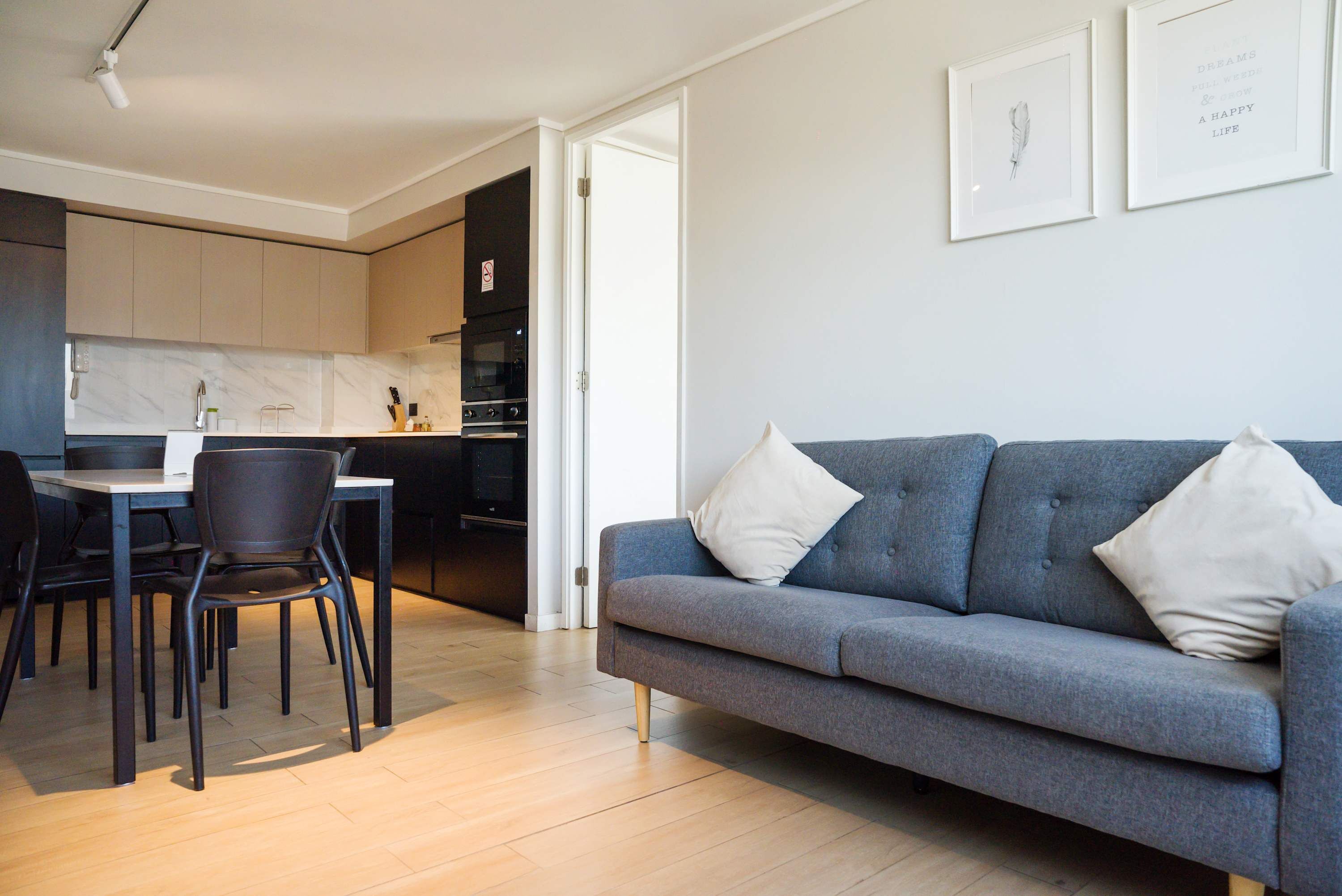 Ein modernes Wohnzimmer mit einem grauen Sofa, zwei Sesseln, einem Esstisch und einer Küche im Hintergrund.