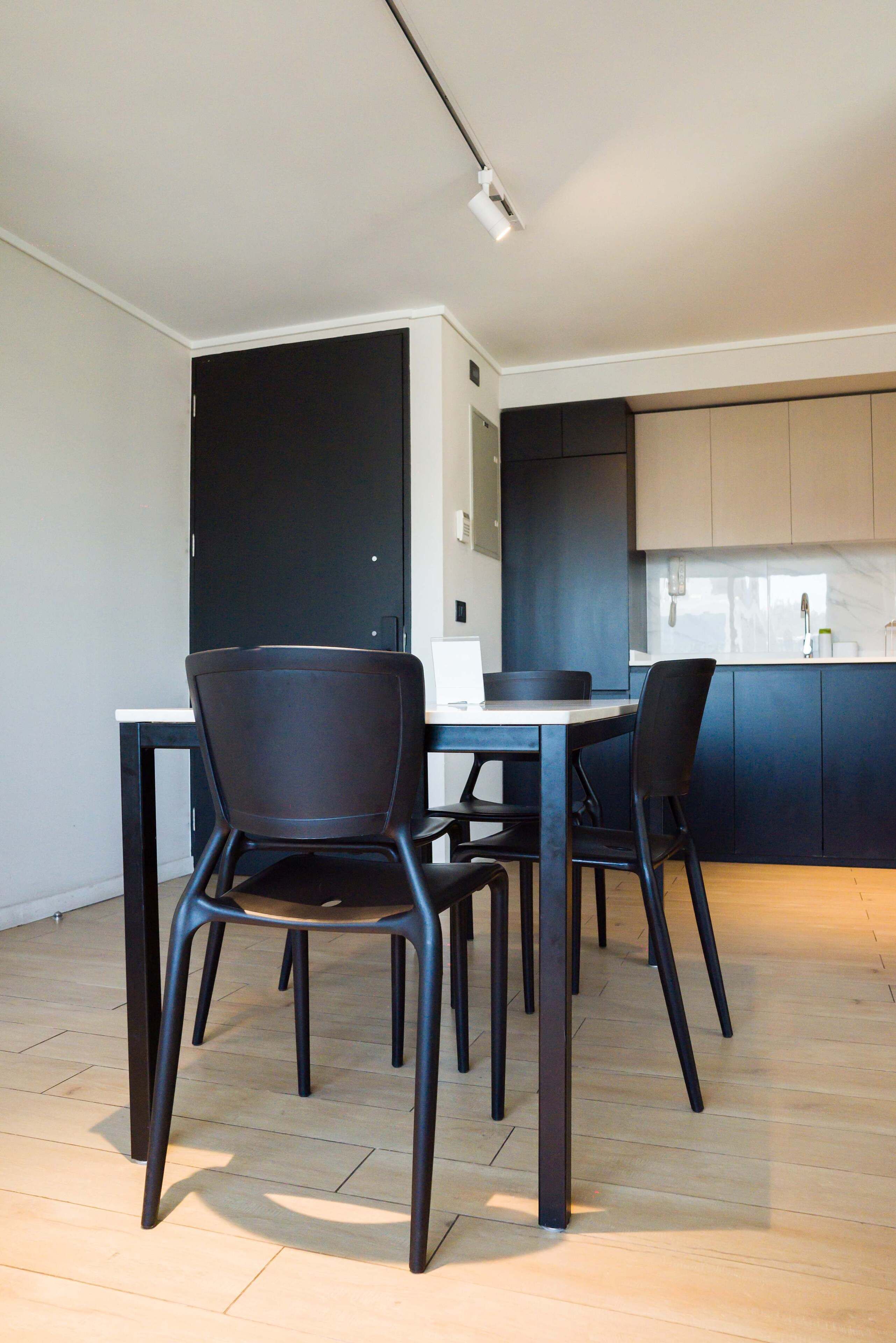 Une cuisine moderne avec des meubles de couleur sombre, un plan de travail blanc et un coin repas comprenant une table et des chaises.