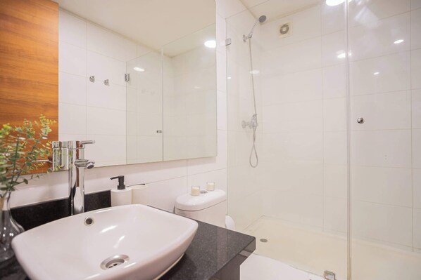 A modern bathroom with a large white sink, a mirror, a shower enclosure, and a toilet.