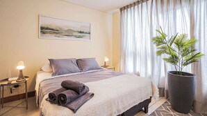 Ett hotellrum med en stor säng, två sänglampor, en tavla på väggen och en krukväxt.