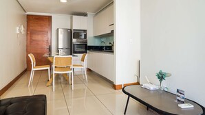 A modern kitchen with white cabinets, a refrigerator, microwave, and oven. There is a dining area with a table and chairs. - Modern Chic Oasis: Sophisticated Las Condes Stay (Las Condes)