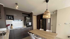 A modern kitchen with dark cabinetry, a wooden dining table, and white chairs. - Viña del Mar: Apartment with sea views and balcony (Viña del Mar)