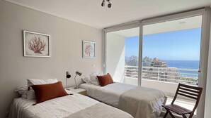 A bedroom with two beds, a wooden chair, and a large window with a city view. - Viña del Mar: Apartment with sea views and balcony (Viña del Mar)