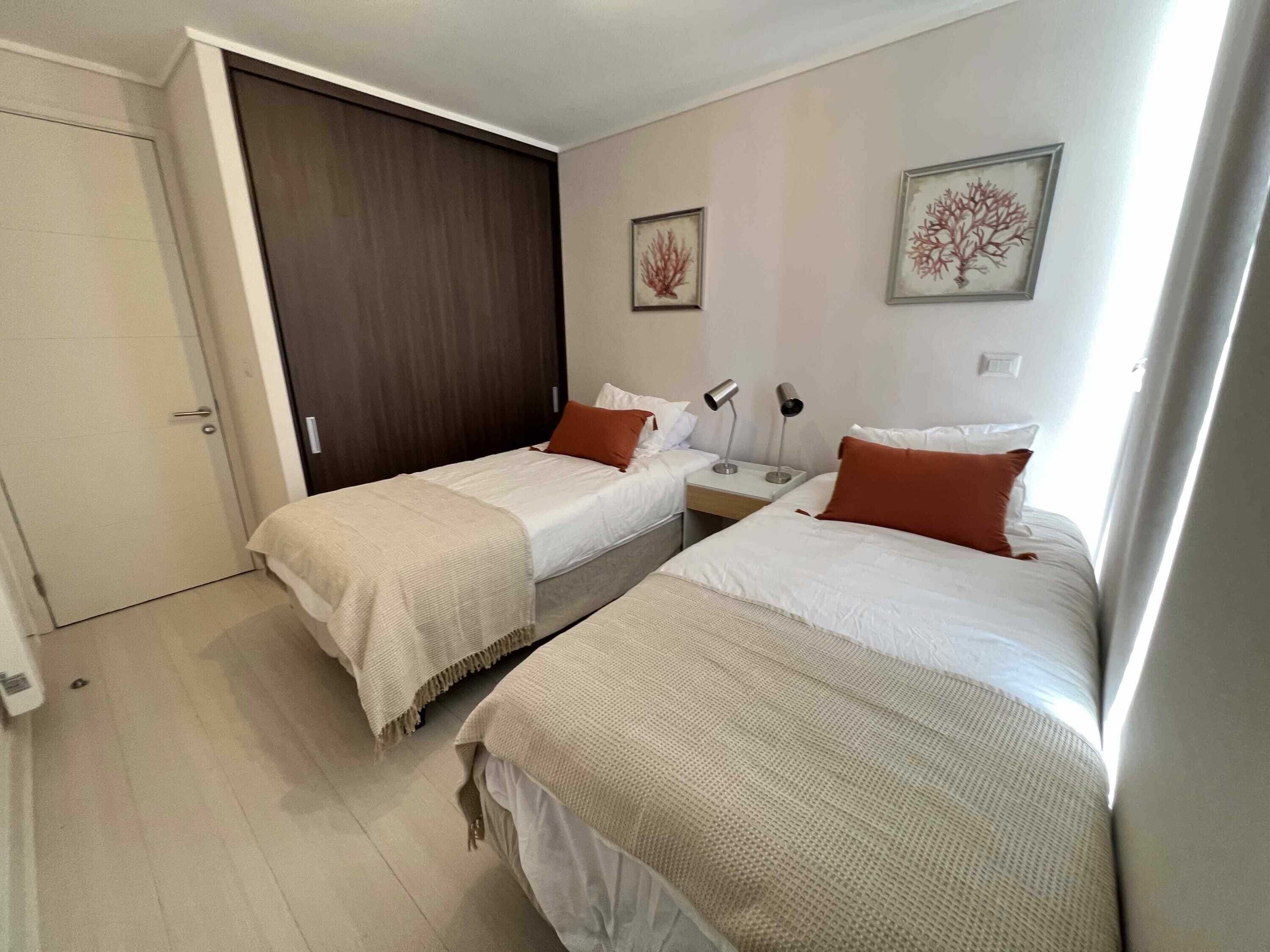 Una camera d'albergo con due letti, un armadio e un comodino con lampade.