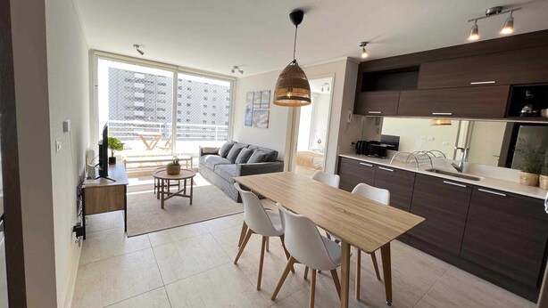 A modern kitchen with dark cabinets, a wooden dining table, and white chairs. - Viña del Mar: Apartment with sea views and balcony (Viña del Mar)