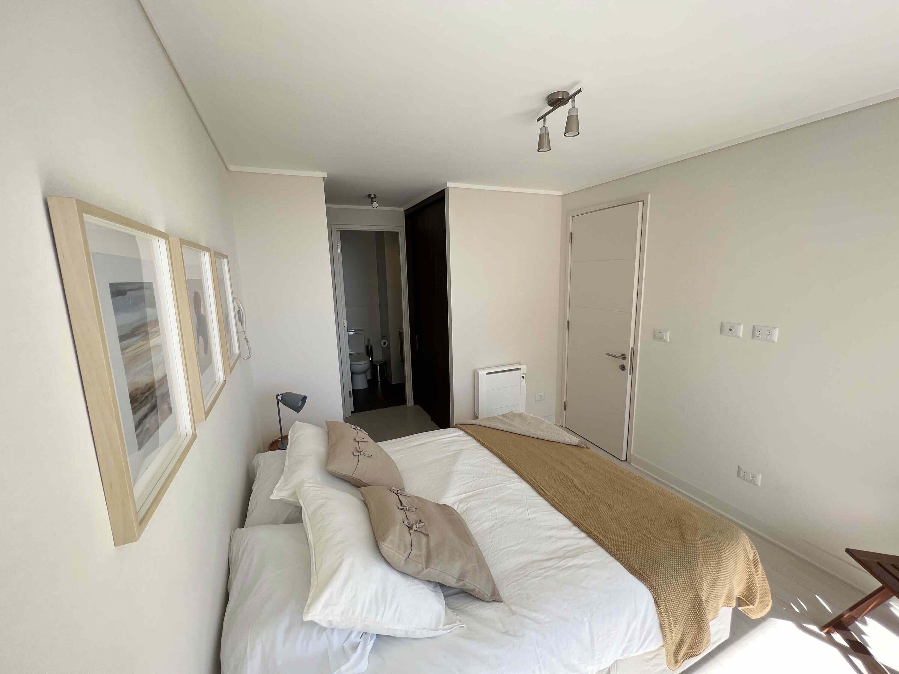 A hotel room with a bed, a bedside lamp, a door, and a wall-mounted light fixture.