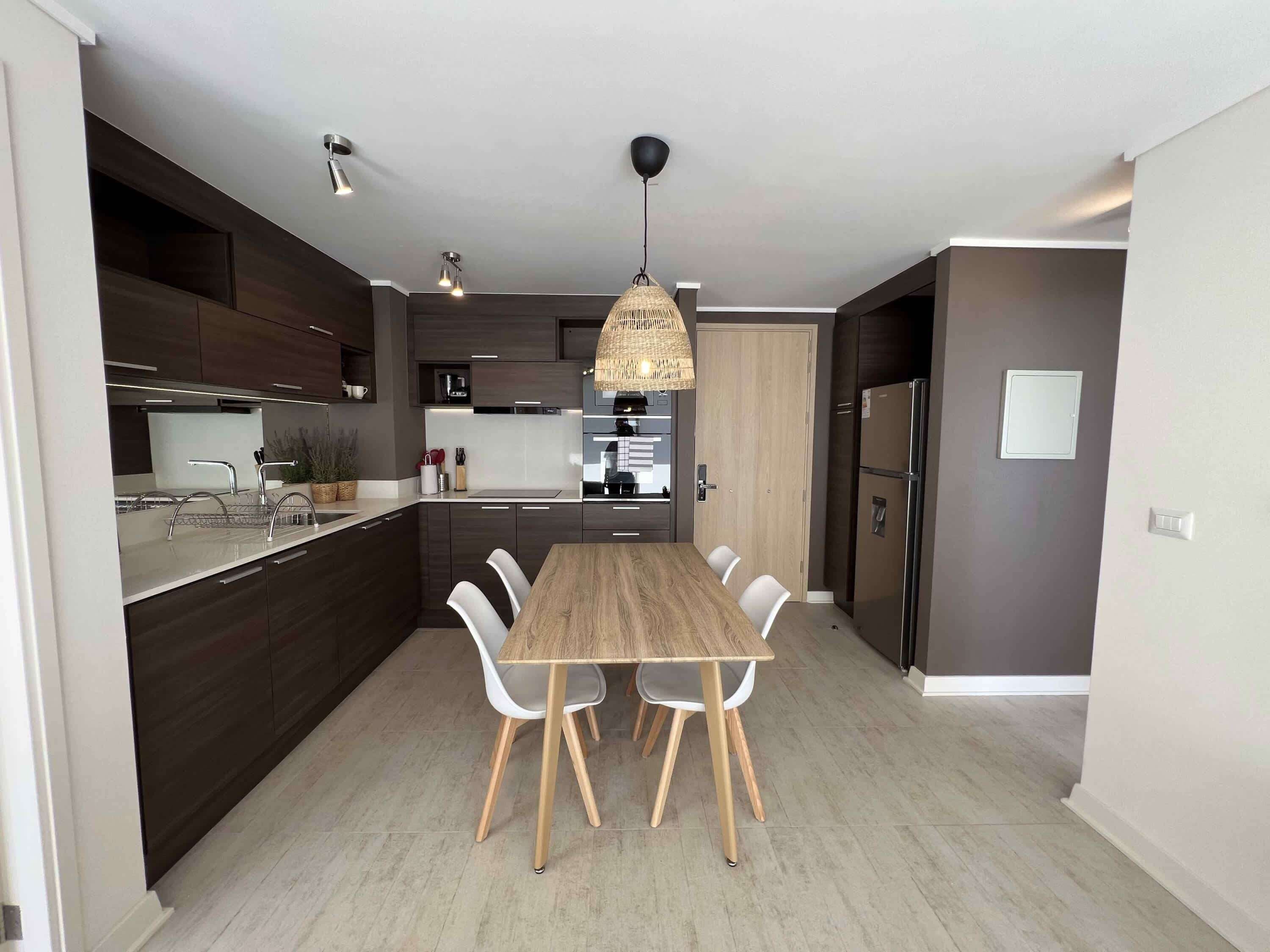 Una cocina moderna con una isla central, sillas blancas y una lámpara colgante.