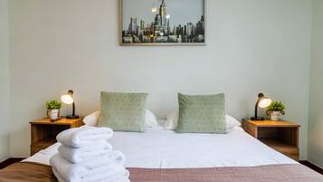 A hotel room with a bed, two nightstands, a framed cityscape picture, and a stack of white towels.