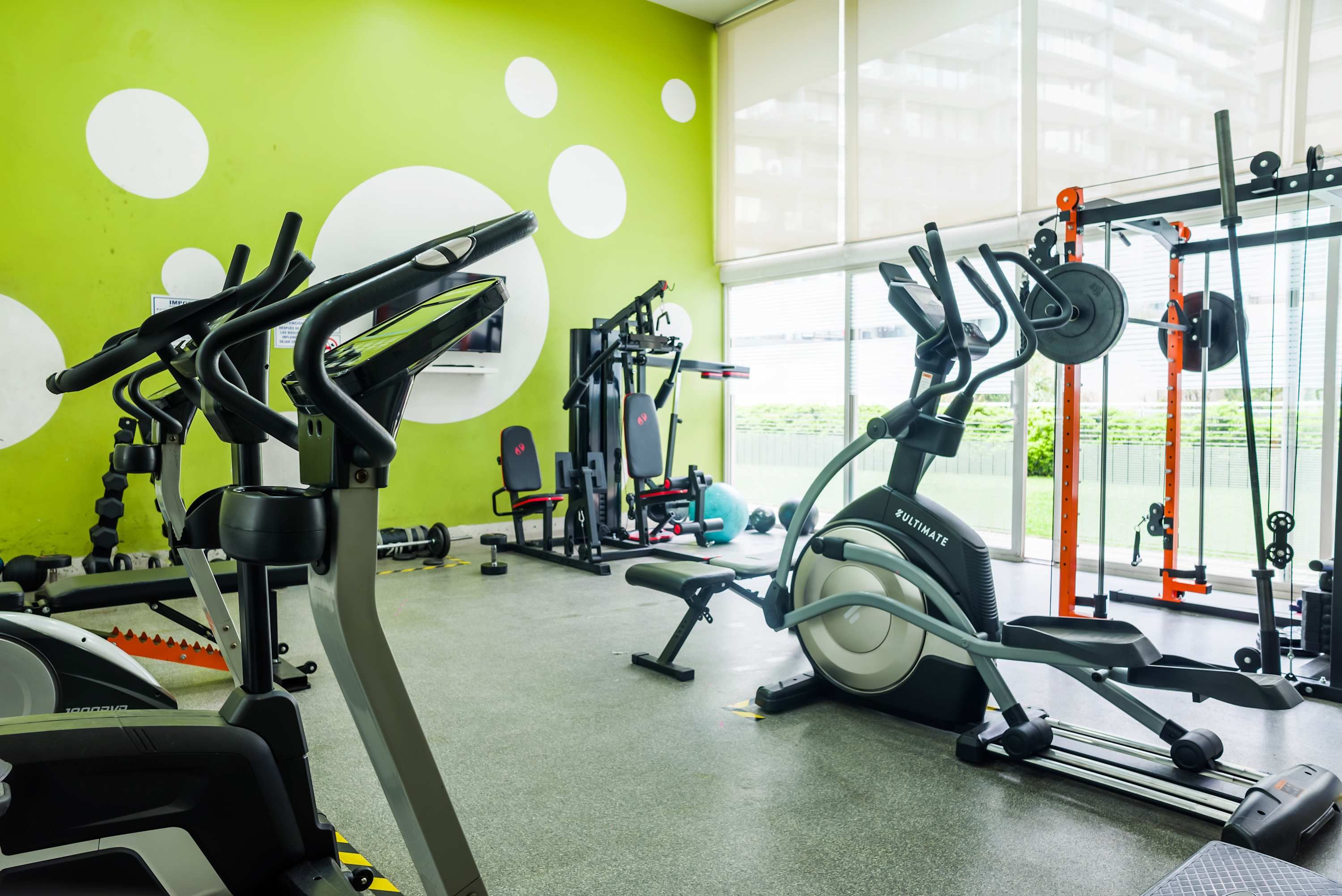 Een sportschool met diverse fitnessapparaten, waaronder een loopband, krachttoestellen en losse gewichten.