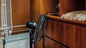 A room with wooden shelving, a standing fan, a white heater, and a bed with a white cover. - Charming Studio in Las Condes with Pool | Ideal 2 (Las Condes)