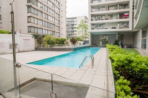 A swimming pool surrounded by a building with multiple balconies and a small garden area. - Cozy Studio In Vibrant Las Condes | 2 Guests (Las Condes)
