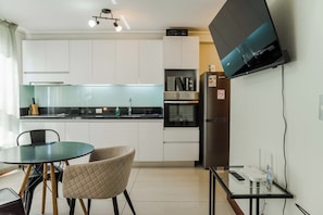 A modern kitchen with white cabinets, a microwave, oven, and a flat-screen TV mounted on the wall.