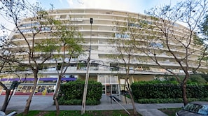 A multi-story building with balconies, a gated entrance, and surrounding greenery.
