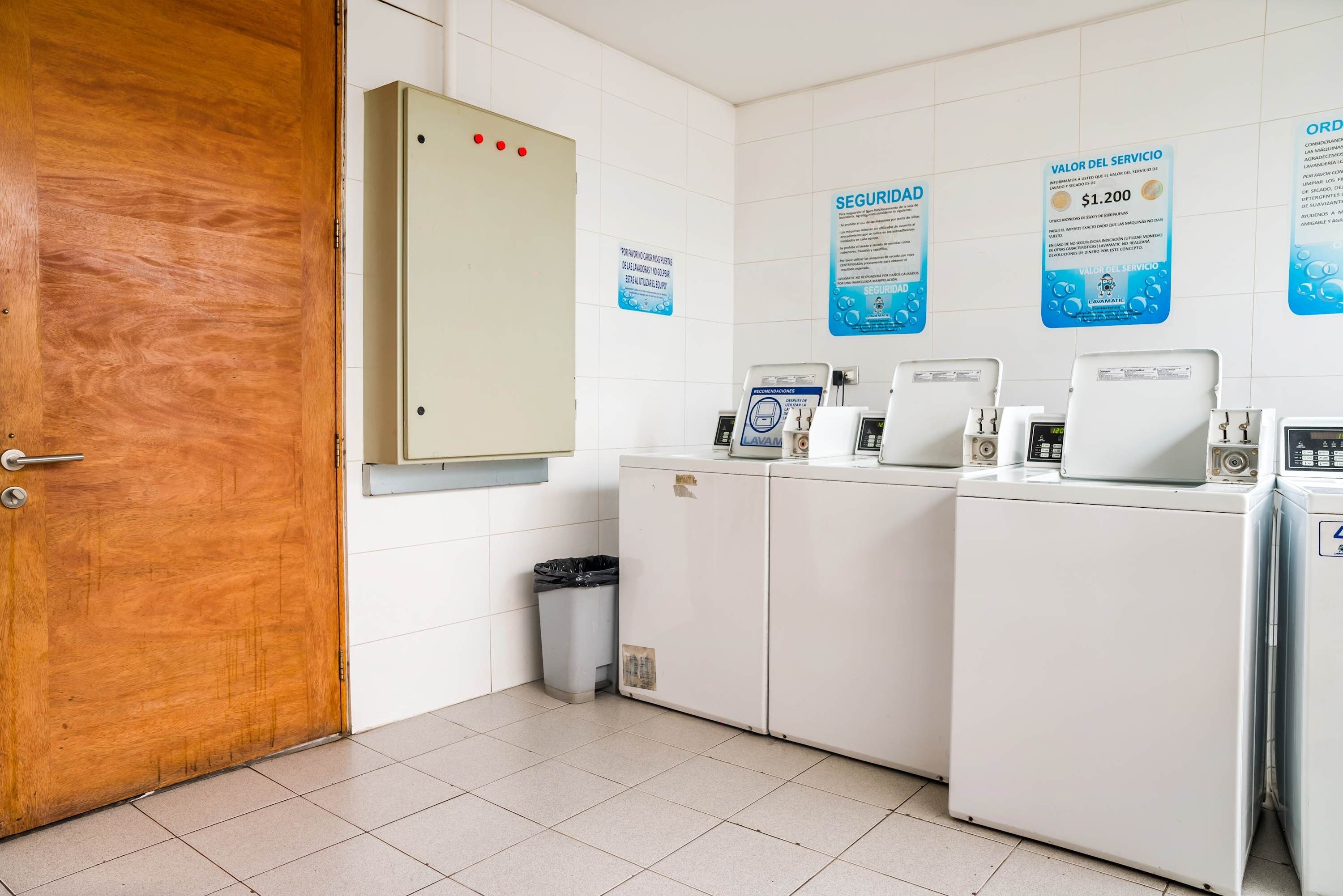 A laundry room with a wooden door, a utility meter, and multiple washing machines.