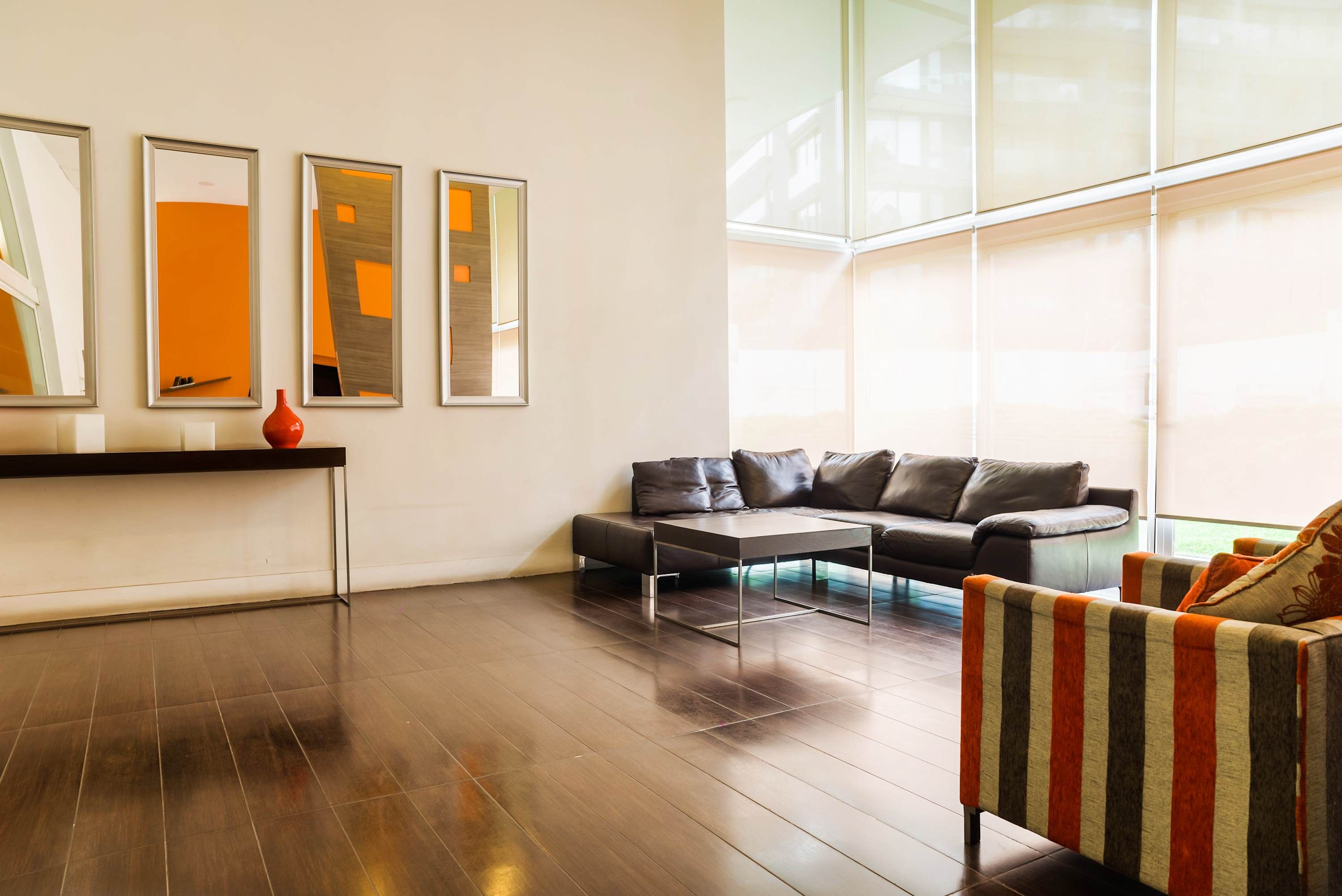 Un salon moderne avec un parquet en bois foncé, un canapé en cuir, un fauteuil à rayures et trois œuvres d’art encadrées accrochées au mur.