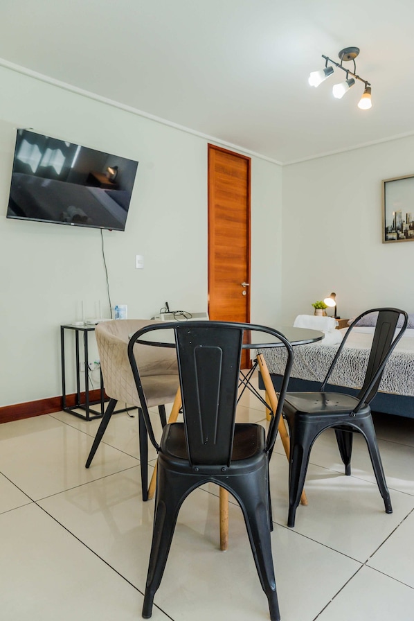 A hotel room with a bed, a desk, a chair, a television mounted on the wall, and a door.