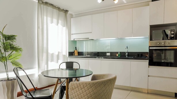 Una cocina moderna con armarios blancos, una mesa de comedor de vidrio y una planta en maceta.