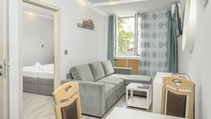 A modern, well-lit room with a grey sofa, a small white table, and a bed in the background.
